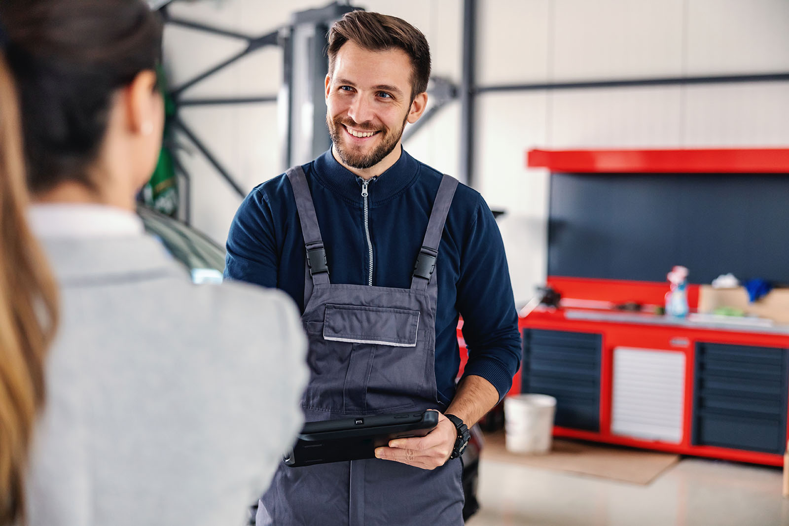 Smiling friendly car seller talking to a mechanic and showing okay hand gesture while standing in car salon. Smiling friendly employe